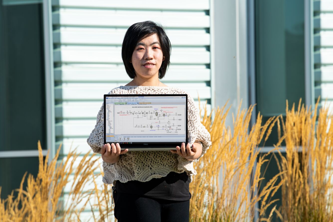 PNNL chemical engineer Yuan Jiang stands outside holding a laptop.