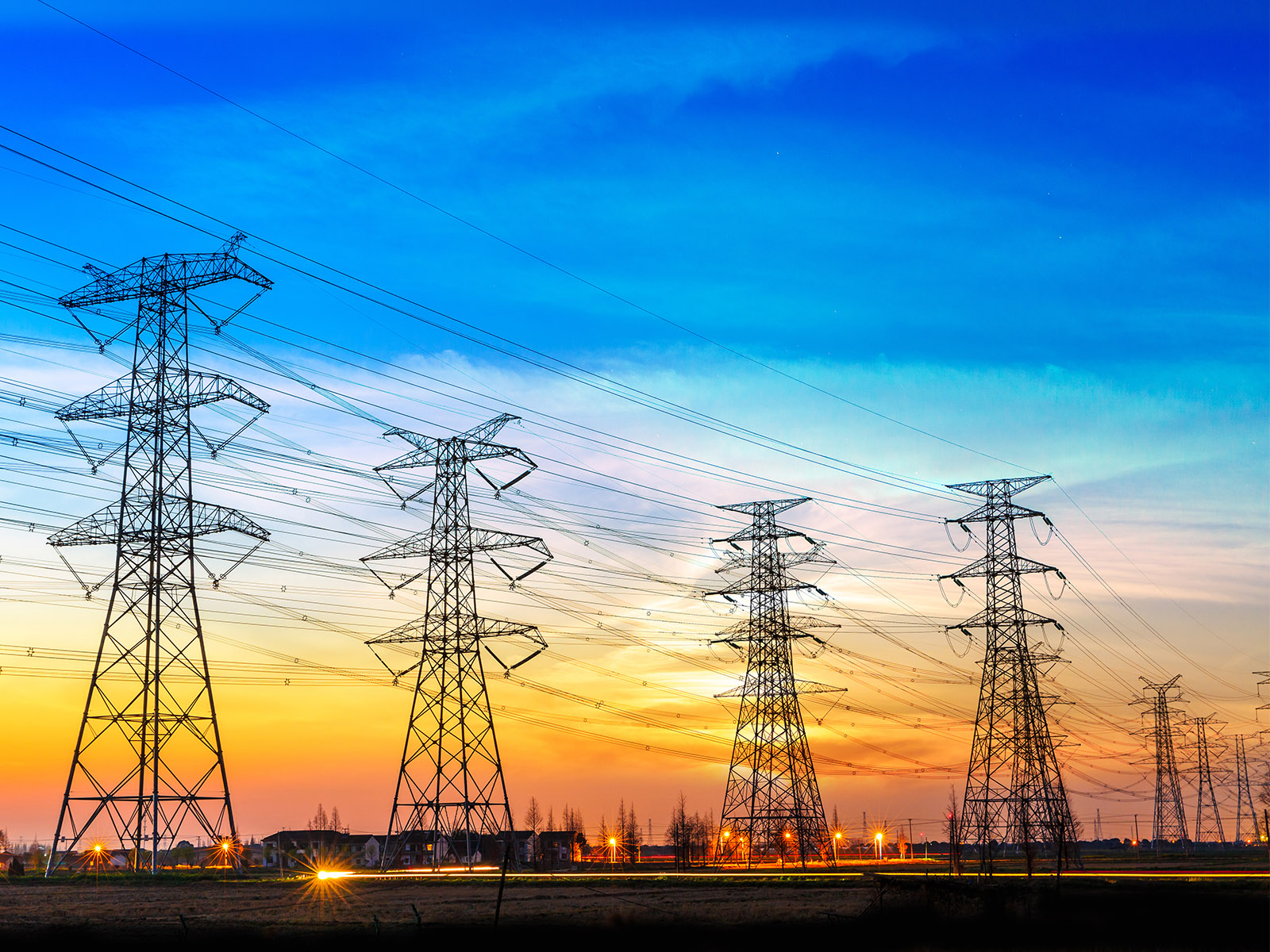 Image of grid transmission lines with a beautiful orange-red sky in the background.