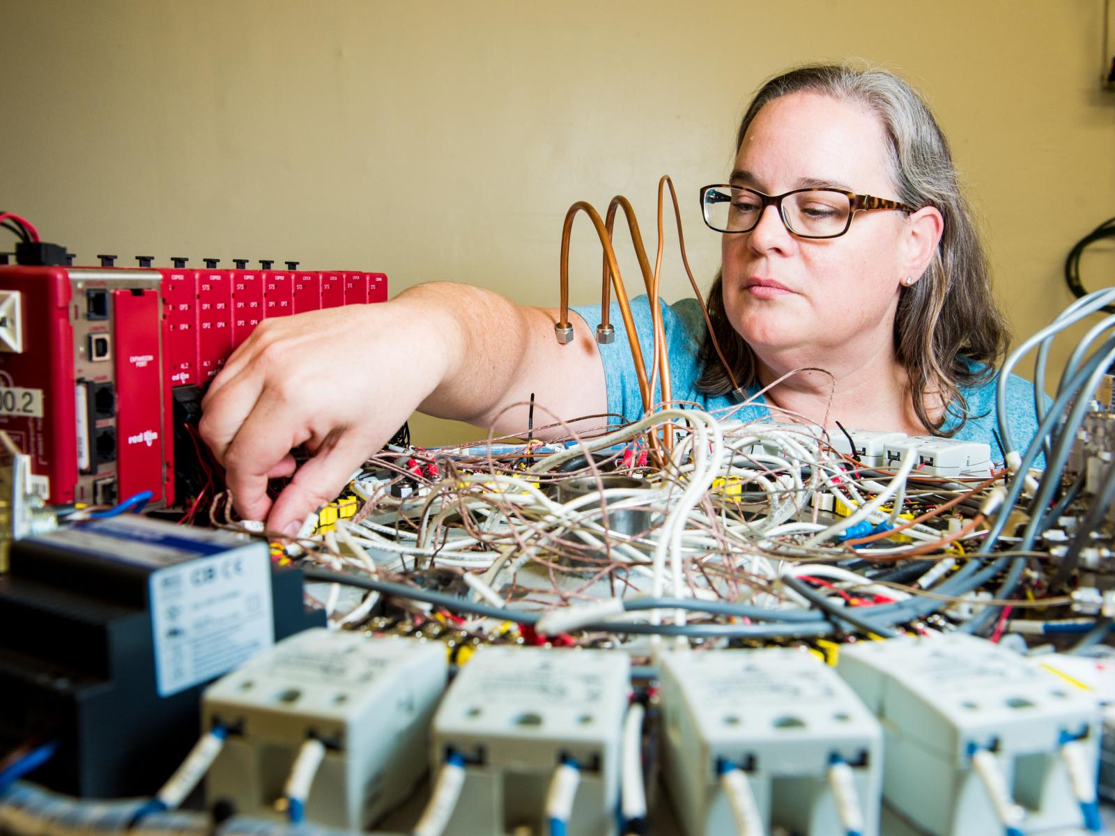 Researcher Heather Colburn reaches across a neck-high platform to connect wires on scientific equipment.