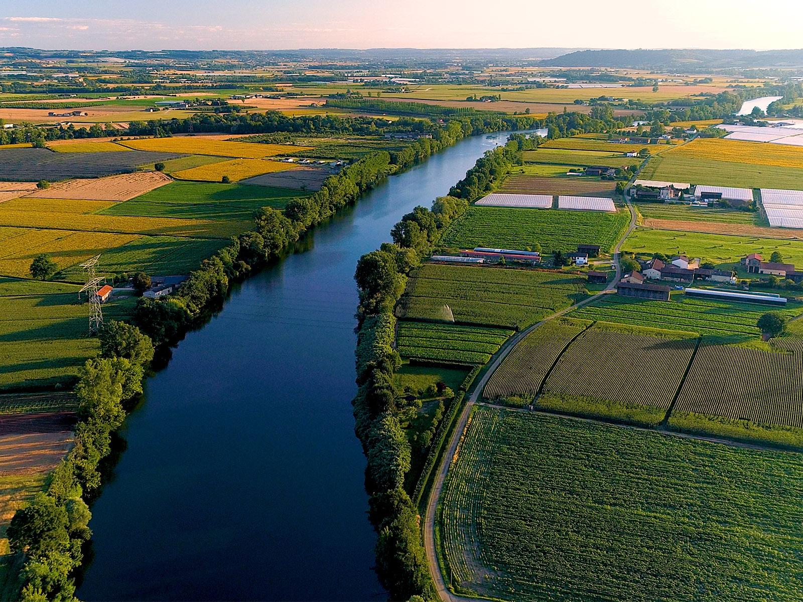 A bright photograph of a river running through agricultural land