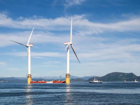 Photo of two floating wind turbines, and ships, at sea.