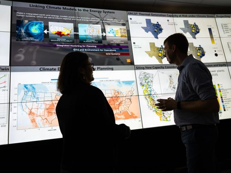Photo of two people standing in front of multiple large monitors that are displaying climate-related information.