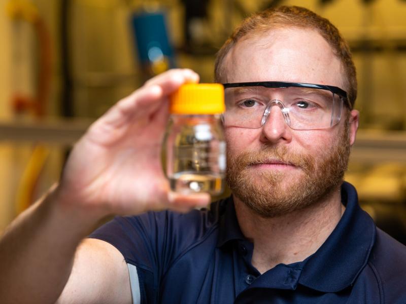 PNNL scientist David Heldebrant holds a glass bottle holding a clear liquid.
