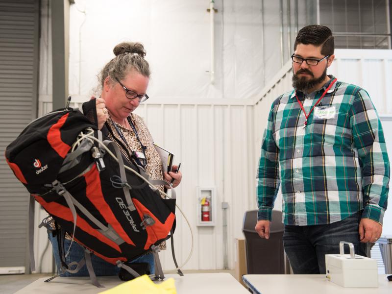 Two researchers prepare to inspect a backpack for contraband