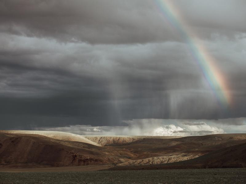 Photograph of clouds and a rainbow over a desert