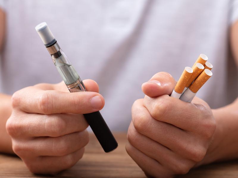 One pair of hands shows an e-cigarette, or vaporizer, and several cigarettes.
