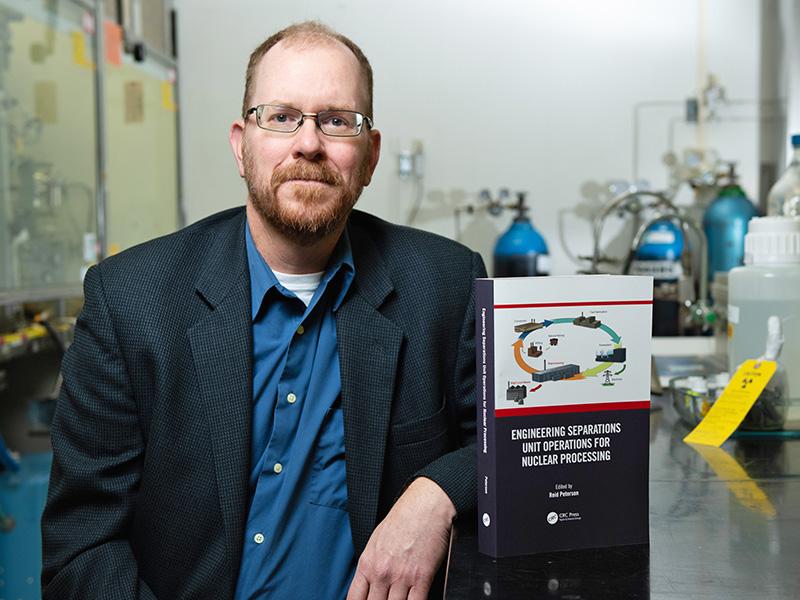Scientist Reid Peterson shows a book about nuclear chemistry while sitting in a research lab.