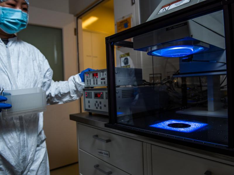 Researcher stands next to a glass box with a blue light
