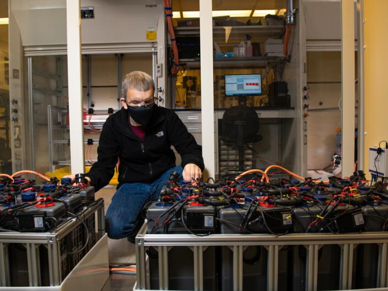 Photo shows a researcher kneeling next to battery testing equipment.